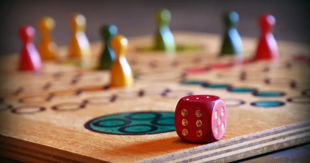 Dado vermelho sobre tabuleiro de madeira com peões coloridos, imagem para plataformas de dado virtual para jogos