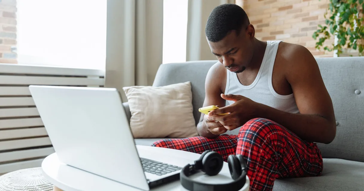 Homem sentado em um sofá com notebook e celular, ilustrando a verificação da velocidade contratada